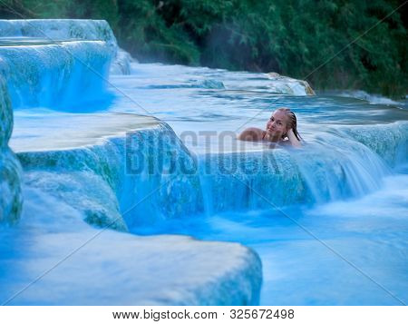 young woman relaxing at natural spa with waterfalls and hot springs at Saturnia thermal baths, Grosseto, Tuscany, Italy