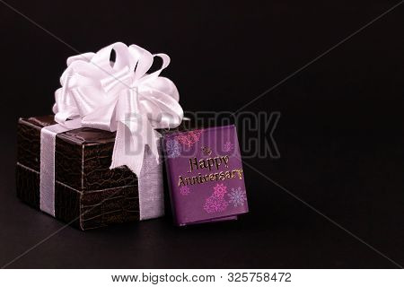 Anniversary Gift Concept. Brown Lether Box Decorated With White Ribbon And Message Diary On Black Ba