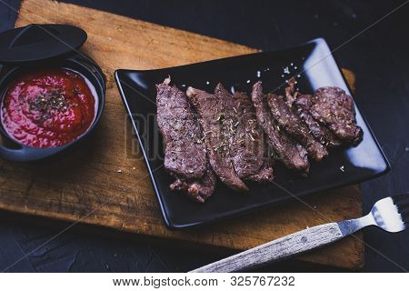 Sliced Grilled Beef Steak. Beef Steak With Tomato Sauce On The Cutting Board On Dark Wooden Backgrou
