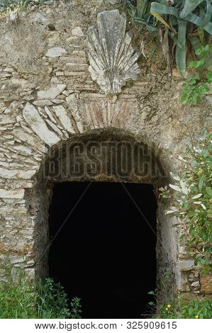 Arched Stone Gate Of Dark Abandoned Cellar With Vintage Decorative Acroterion Ornament.