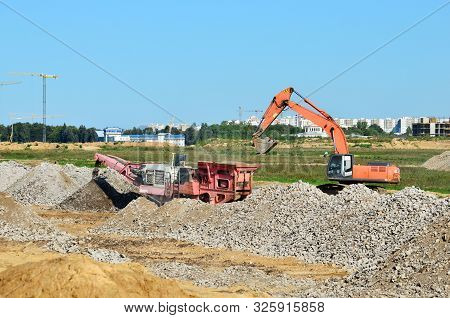 Heavy Tracked Excavator Load Stone, Old Asphalt Or Concrete Waste Into A Mobile Jaw Crusher Machine.