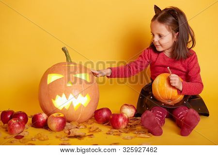 Indoor Shot Of Cute Dark Haired Girl Sitting On Floor Over Backgroundof Autumn Scenery In Studio. Au