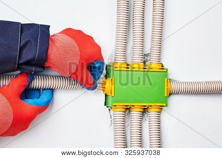 An Electrician Connects An Electric Conduit To A Square-shaped Distribution Box Made Of Green Plasti