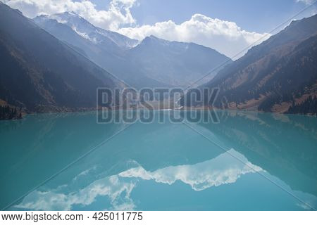 Mirror Of The Big Almaty Lake With Reflection High In The Mountains With Snow-capped Peaks And A Sky