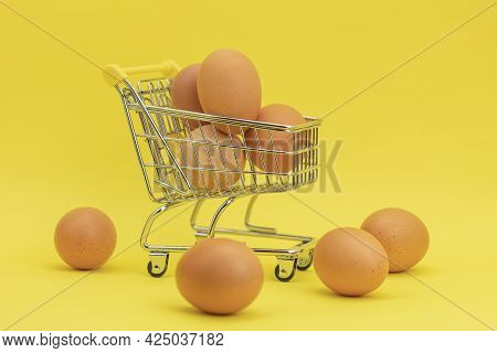 Raw Chicken Eggs In A Basket On A Yellow Background. Eggs In A Metal Cart On A Yellow Background. Ba