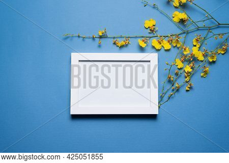 Blank Empty Picture Frame With Copy Space And Oncidium Orchid Flowers Branch On The Blue Flat Lay Ba