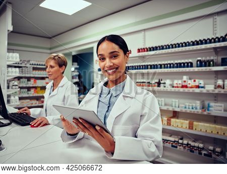 Portrait Of Smiling Young Female Pharmacist Wearing Labcoat Holding Digital Tablet With Senior Colle