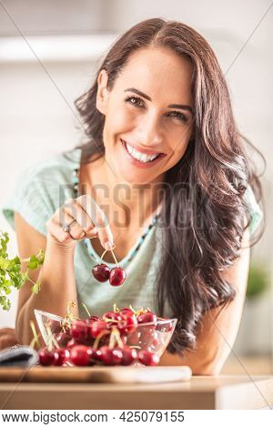 Smiling Woman Picks Two Cherries From A Seethrough Bowl Indoors.