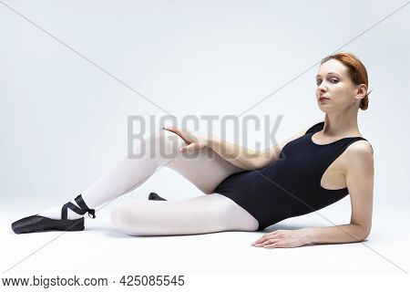 Proudly Looking Gorgeous Professional Female Ballet Dancer In Body Suit Posing On White Floor.