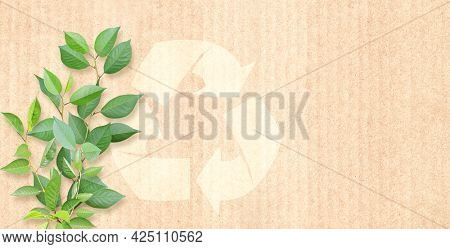 Arrows recycle symbol and green leaves on cardboard texture. Horizontal banner with eco paper texture. Paper cardboard background. Recycled carton material. Copy space for text. Mock up template