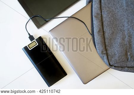 Gray Backpack With Fashionable Silver Laptop Or Ultrabook, Tablet And An Power Bank Lie On A White B