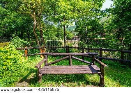 Wooden Bench In A Park Next To A Mountain Stream.