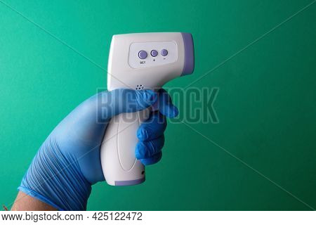 Man's hand wearing nitrile gloves holding infared o thermometer green background         