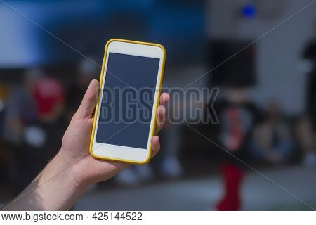 The Guy Holds A Mock-up Of A Smartphone In His Hand Against The Background Of The Children's Dance C