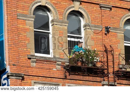 Auckland New Zealand - June 19 2021; Woman In Blue Tends Flower Through Window In Traditional Red Br