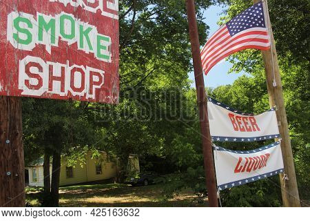 Smoke Shop Sign Next To Beer And Liquor Sign With American Flag. Rural Texas Scenery. Small Town Tex