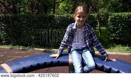 Blonde Girl Playing At Playground, Child Spinning, Rotating On Merry-go-round In Park, Face Of Happy