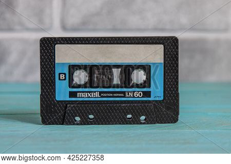 Krasnodar, Russia - March 11, 2021: A Black Maxell Audio Cassette Stands On A Blue Wooden Background