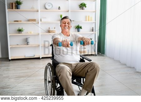 Joyful Disabled Man In Wheelchair Making Rehabilitation Exerises With Dumbbells At Retirement Home