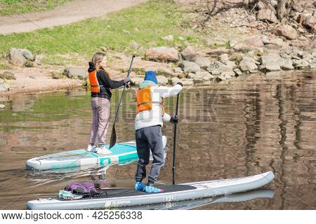 Vyborg, Russia, May 2, 2021-young Women In Sports Outfit And Orange Life Vests Surf On Supboards In 