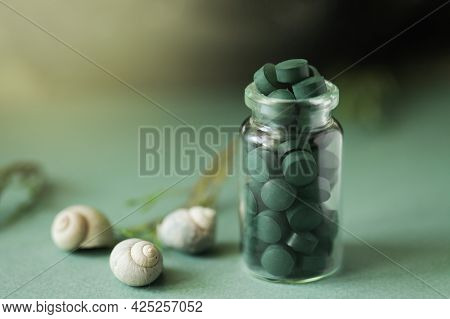 Spirulina Pills In Glass Bottle, Sea Shells On Green Background. Antioxidant Nutrition. Bio-energy, 