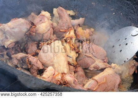 Large Pieces Of Lamb Meat With Lamb Fat Dumba Close-up Fried In Oil With Bubbles In A Black Cauldron