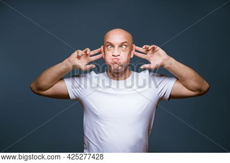 Comic Bald-headed Male Posing On A Blue Background With Excited Facial Expressions And Raised Hands 