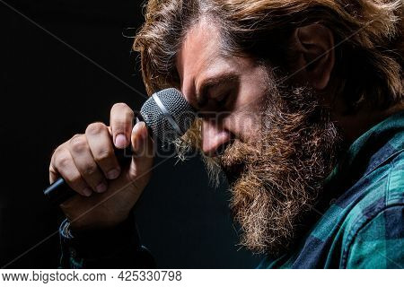 Male Singing With A Microphones. Man With A Beard Holding A Microphone And Singing. Bearded Man In K