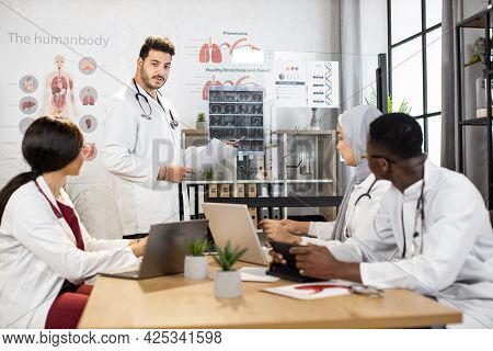 Group Of Four Multiethnic Doctors Having Consilium At Hospital For Examining Tomography Of Severe Pa