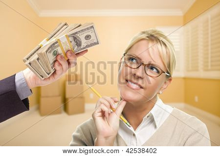 Mulher segurando o lápis, sendo entregue a pilha de dinheiro em uma sala vazia com caixas.