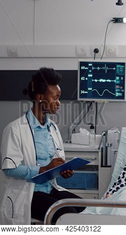 Afro American Doctor Writing Medical Expertise On Clipboard Monitoring Disease Symptom Working In Ho
