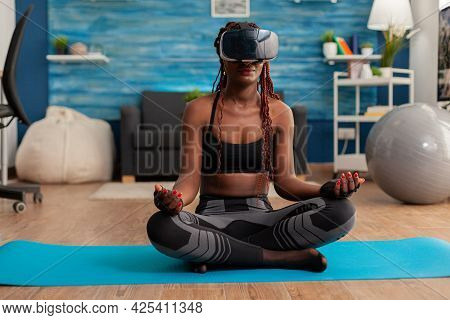 Calm Tranquil Black Woman Wearing Vritual Reality Goggles Sitting On Yoga Mat, Spending Time On Spir