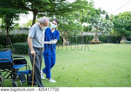 Asian Young Woman Nurse Taking Care And Support Disabled Senior Elderly Man On Wheelchair At Backyar