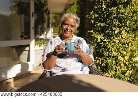 Portrait of smiling senior african american woman having tea in sunny garden. retreat, retirement and happy senior lifestyle concept.