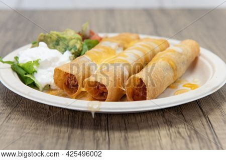 Three Crispy Deep Fried Chicken Taquitos Covered With Melted Cheese And Served With A Scoop Of Sour 