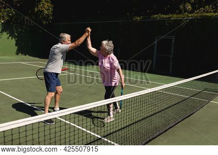 Senior caucasian couple playing tennis together on court highfiving. retirement retreat and active senior lifestyle concept.