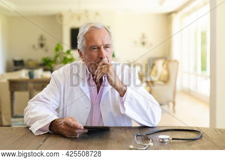 Senior caucasian male doctor sitting at table using tablet computer. medicine and healthcare services concept.