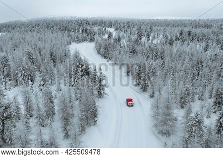 Drone view of a red car driving though a snowy forest in Lapland, Finland