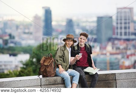 Young Couple Travelers With Map In City On Holiday, Using Smartphone.