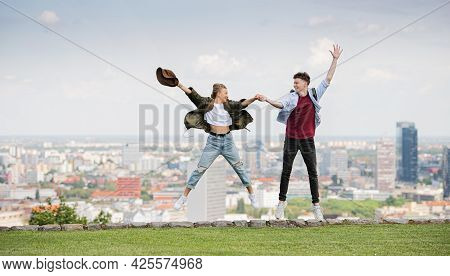 Cheerful Young Couple Travelers In City On Holiday, Jumping. Cityscape In The Background.