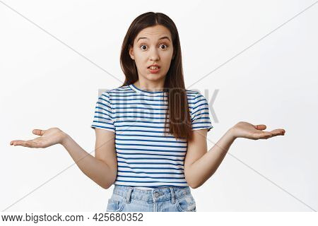 Sorry I Didnt Know. Clueless 20s Woman Shrugging Shoulders, Spread Empty Hands Sideways And Look Con