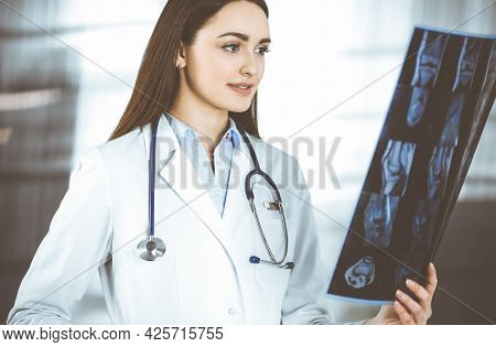 Professional Young Woman-doctor Is Looking At Her Patients Roentgenogram. Physician At Work In A Cli