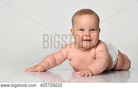 Happy Portrait Six Month Old Baby Girl In A Diaper Lying Sly Looking At You, Arms Outstretched To Th