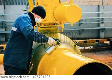 A Painter In Working Clothes Paints A Metal Shut-off Valve For Gasification From A Compressor Gun On
