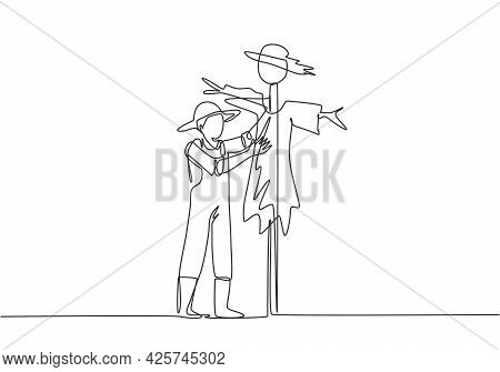 Continuous One Line Drawing A Young Male Farmer In A Straw Hat Is Putting Up A Scarecrow To Keep Out