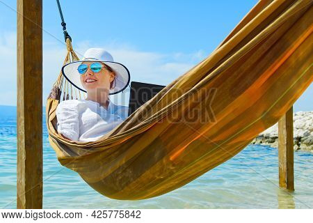 Work From Anywhere. Young Smilyng Woman, Female Freelancer In Straw Hat Working On Laptop On Beach.