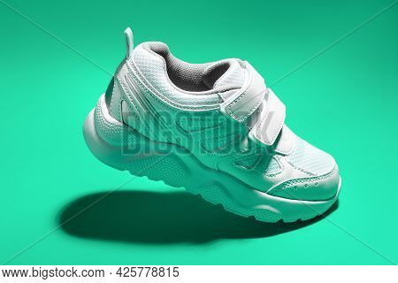 One Macro Flying White Teen Sneaker With Velcro Fasteners Isolated On A Green Background In A Minima