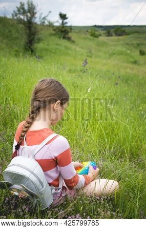A Little Cute Girl Is Sitting On The Grass With A Pop It - Antistress Toy.