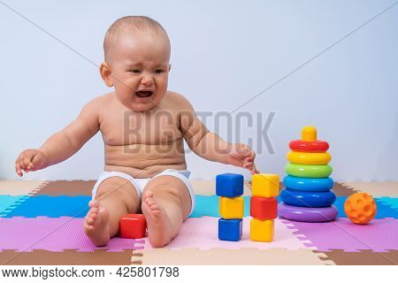 A Toddler Cries While Sitting On The Floor In The Playroom Among Toys.