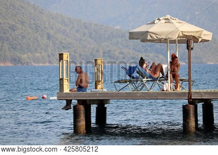 Hisaronu, Turkey​ -​ July 2021: People Sunbathing On A Beach On Green Mountains Background. Tourists